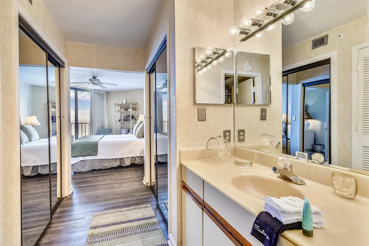 A serene bathroom scene with a well-lit vanity, mirrored cabinets for storage, and an open doorway leading toward a bedroom. The calm atmosphere and soft natural light emphasize the comfort and convenience of the bathroom spaces.