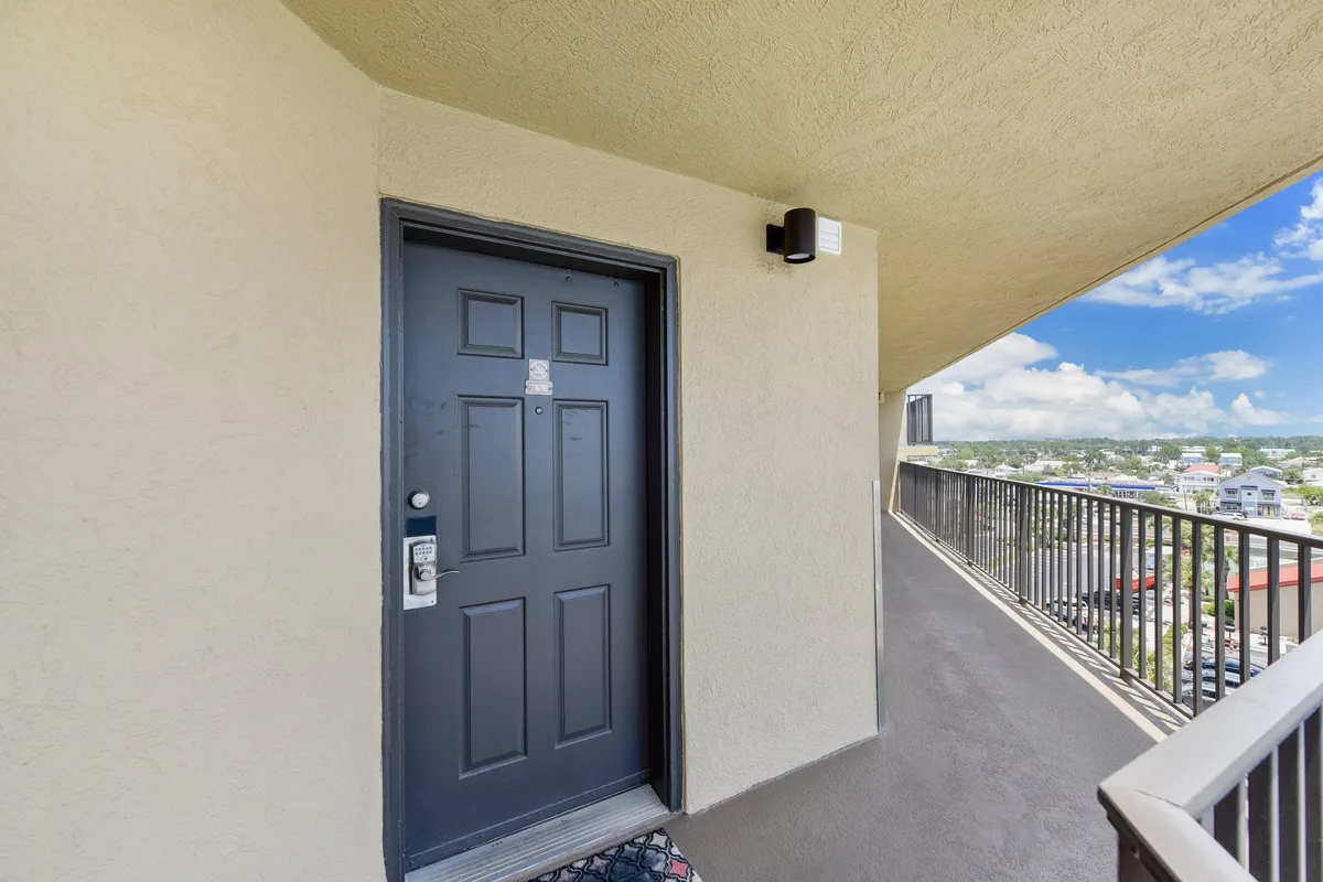 The front door and balcony of a condo, with a view hinting at the ocean beyond. The space looks welcoming, perfect for relaxing with friends on the balcony or greeting guests before heading out.