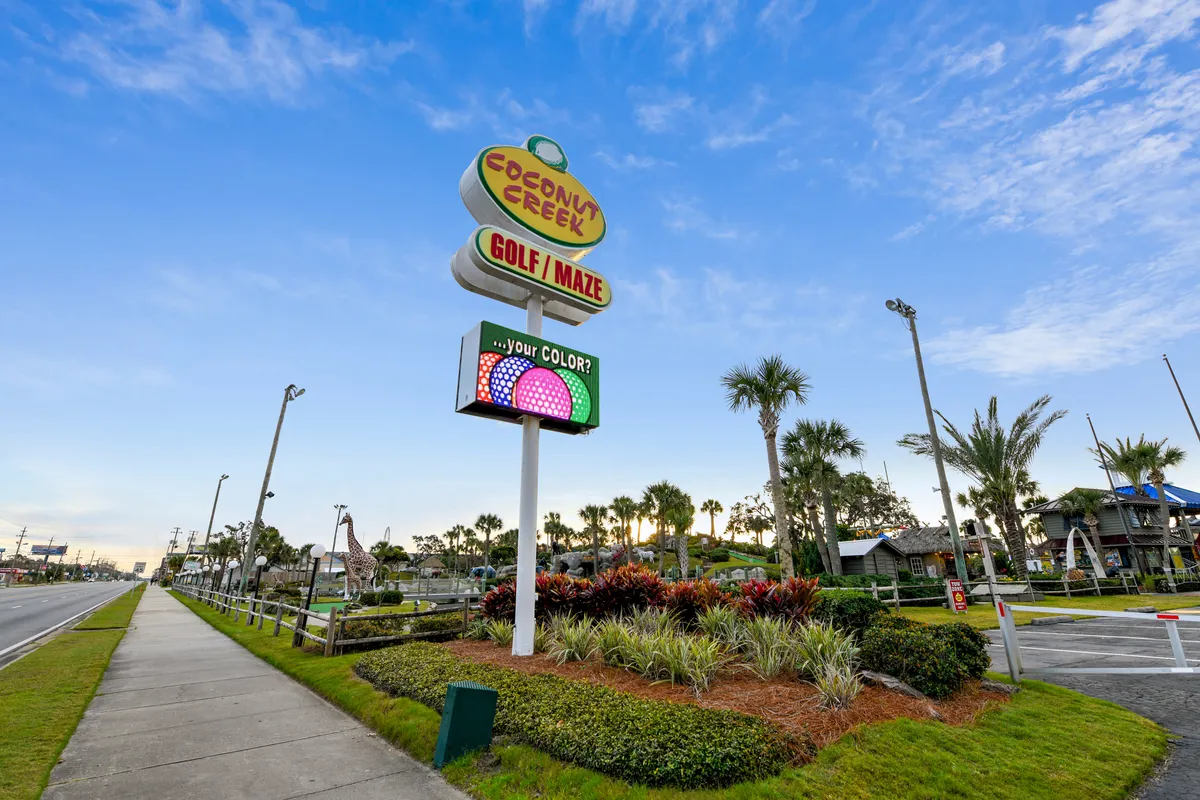 This lively exterior image captures the welcoming sign for Coconut Creek Golf / Maze, a giraffe statue, palm trees, and playful miniature golf course structures. The scene is bright and fun, inviting families to enjoy outdoor games and create joyful vacation memories together.
