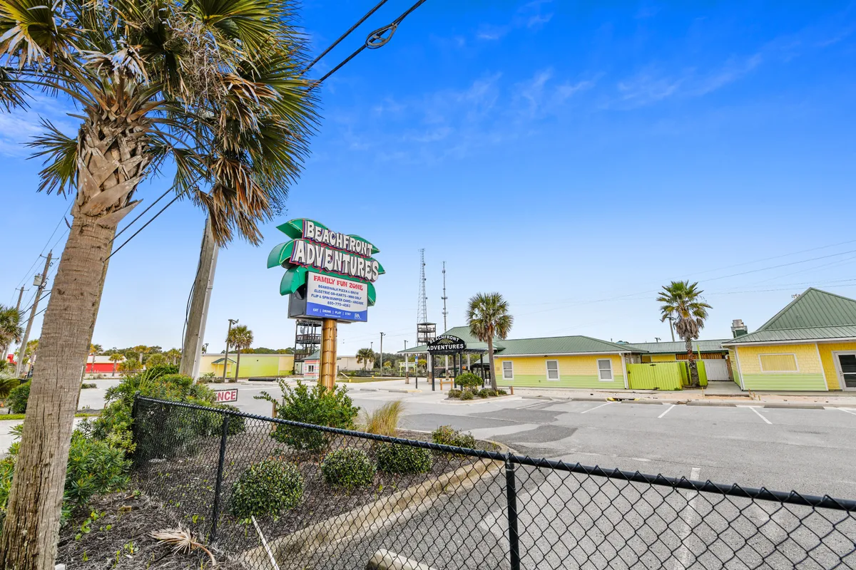 A cheerful scene with the Beachfront Adventures sign, palm trees, and colorful buildings in the background. The area is inviting for families and suggests a variety of fun activities and leisure opportunities nearby.